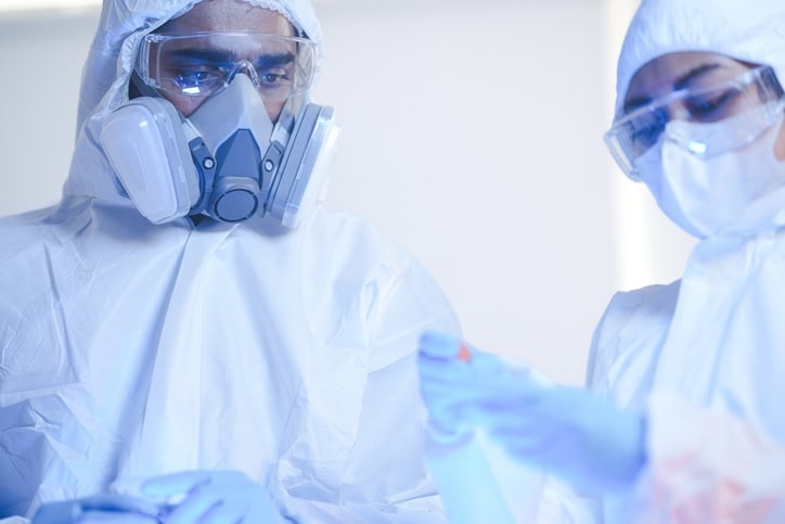 A frontline team of scientists in full protective hazmat suits follows strict protocols in a sterile laboratory. Concept for teamwork, safety, and scientific procedure